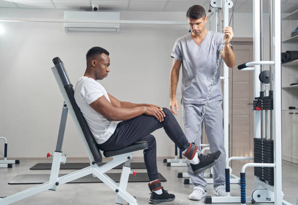 Pic3 Serious concentrated young man performing seated leg raise assisted by experienced kinesiologist